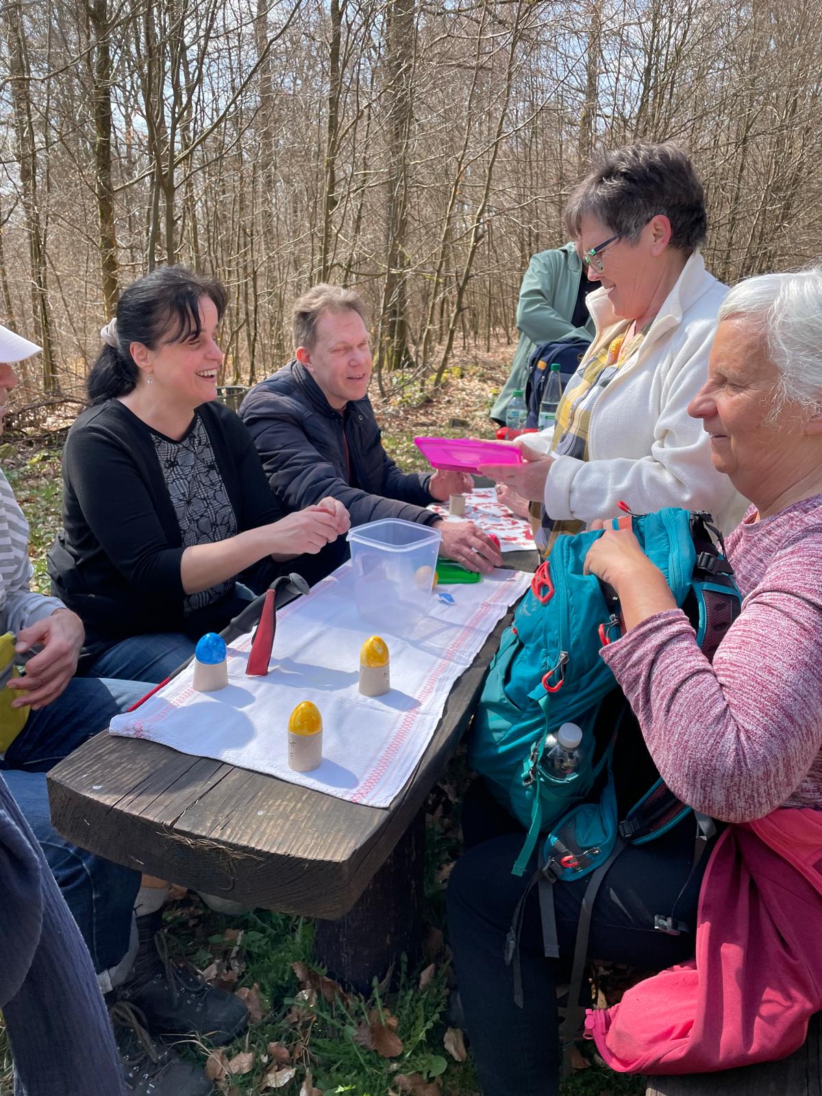 Die Gruppe sitzt an einem österlich gedeckten Tisch in Waldumgebung. Die Stimmung ist fröhlich.